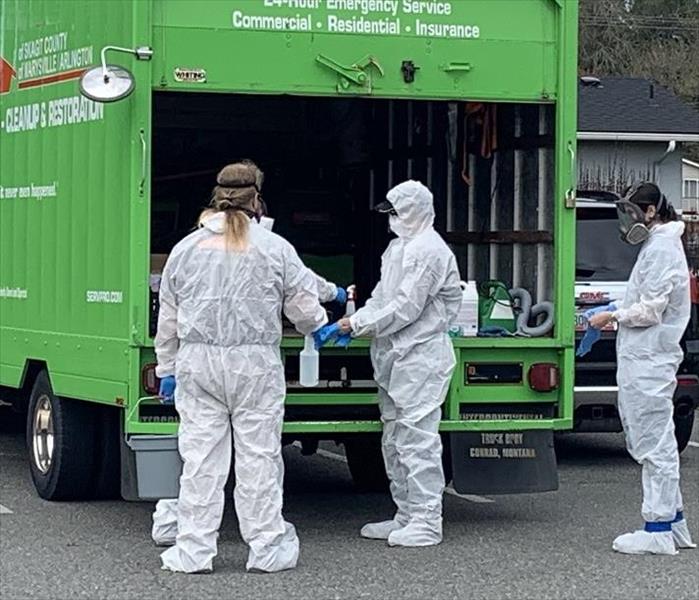 SERVPRO technicians behind open SERVPRO truck donning PPE equipment