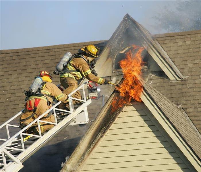 Firemen on ladder reaching fire on roof