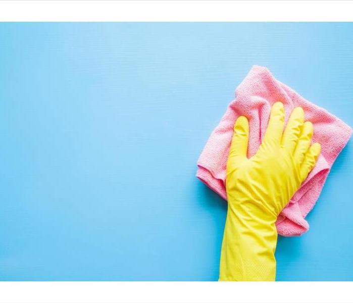 yellow gloved hand wiping a blue wall with a pink rag